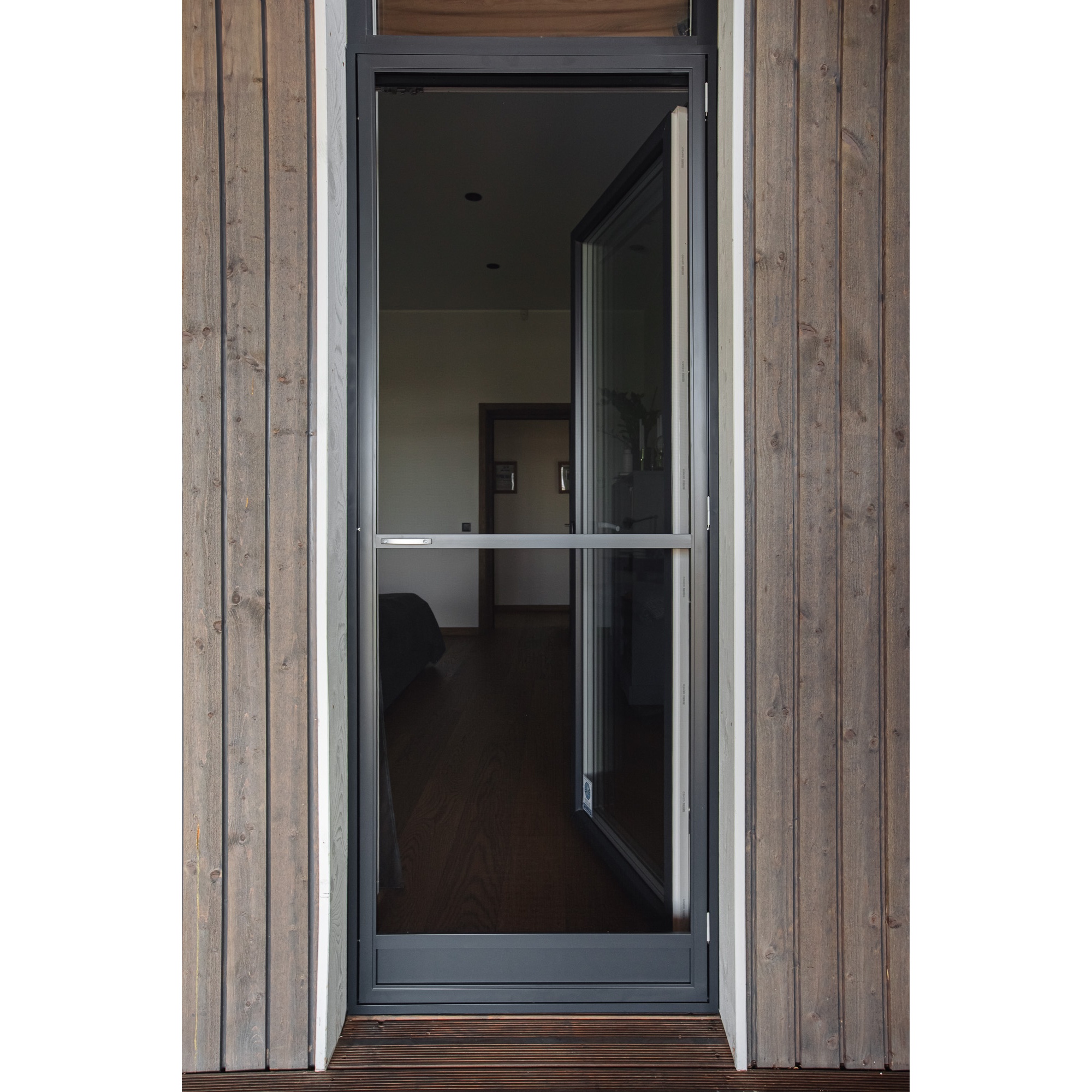 En Myggnät dörr - öppningsbar med en mörk metallram är placerad i en trävägg och visar det inre rummet genom sitt glas.